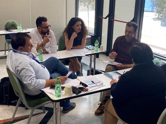 Group of course participants is sitting in a circle and debating engaged. 5 peole are seen. 2 Women 3 men. 