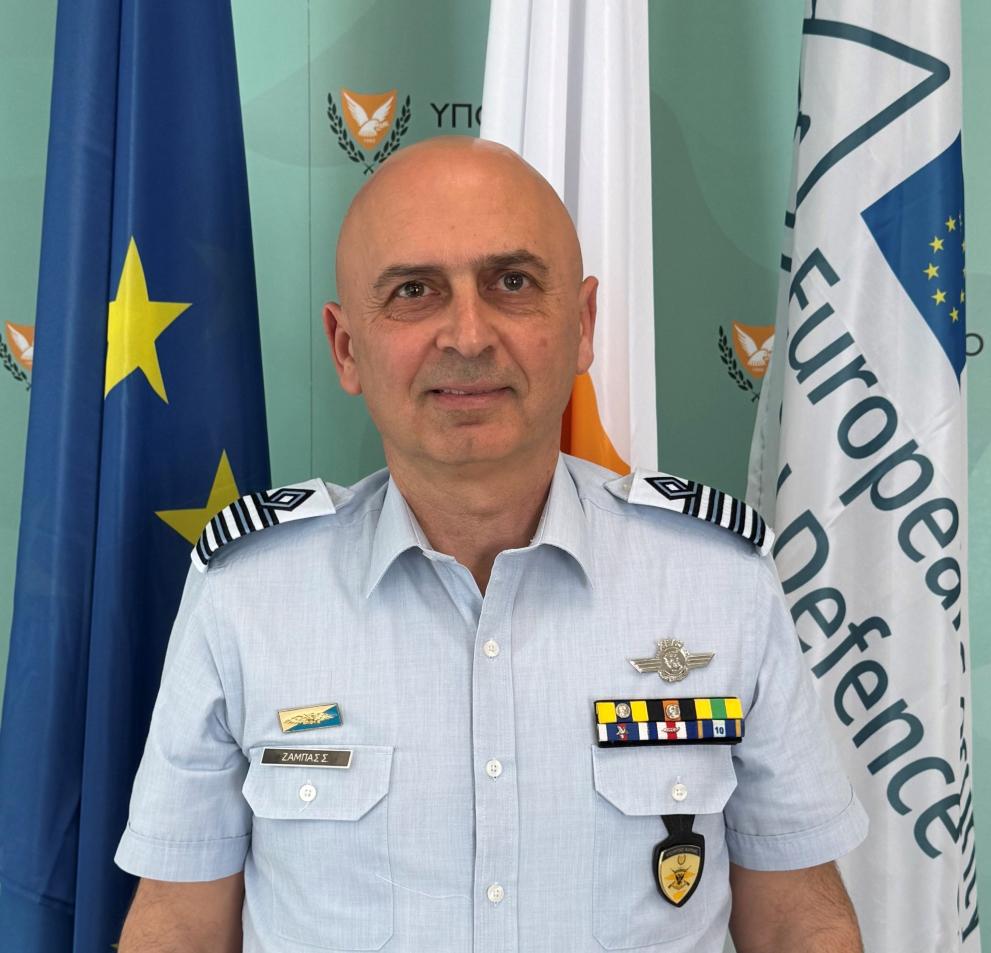 Col Symeon Zambas in uniform of the Cyprus Air Command infront a ESDC and Europe Flag. Light smile 