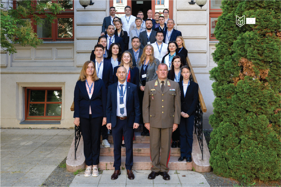 Group Picture of ca. 20 people on stairs. All formally dressed. Man in uniform in front. Bushes on the right.