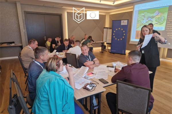 Group of participants around a table discussing. EU roll-up in the background.